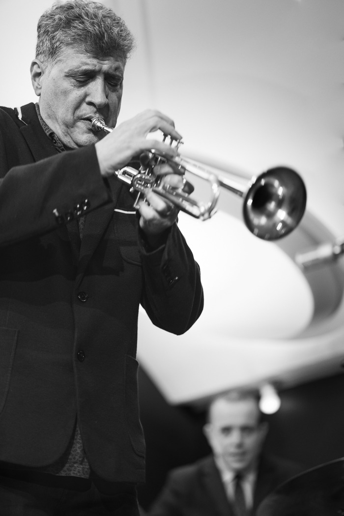 A man playing the trumpet in front of an airplane.