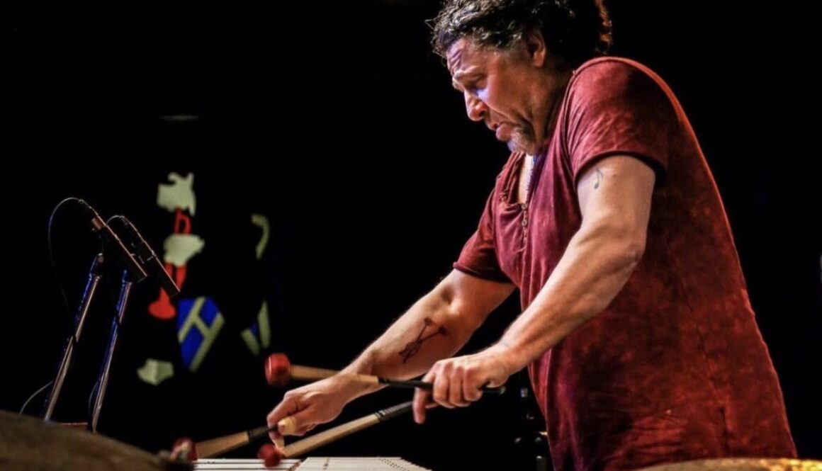 A man playing drums on stage with other people.